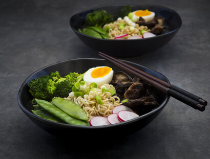 Ramen soup with egg, sugar peas, broccoli, noodles, shitake mushroom and red radish in a black bowl
