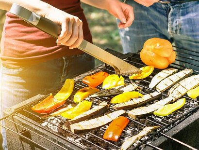 Young woman cooking vegetables for vegetarian barbecue dinner outdoor - Couple grilling peppers and aubergines for bbq - Vegan and healthy lifestyle concept - Soft focus on bottom barbecue tongs