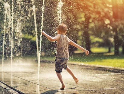 Junge spielt mit den Wasserfontänen