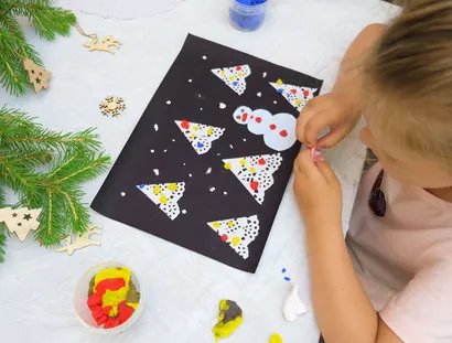 Junges Mädchen bastelt Weihnachtskarte mit Schneemann und Weihnachtsbaum aus Vogelperspektive