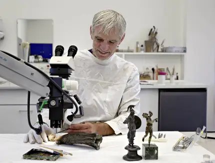 Restaurator Uwe Peltz bei der Reinigung einer römischen Bronzestatuette der Minerva von Korrosion.