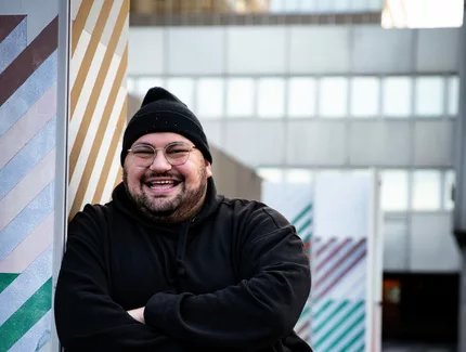 BORA mit Mütze und Winterjacke an einer Wand lehnend