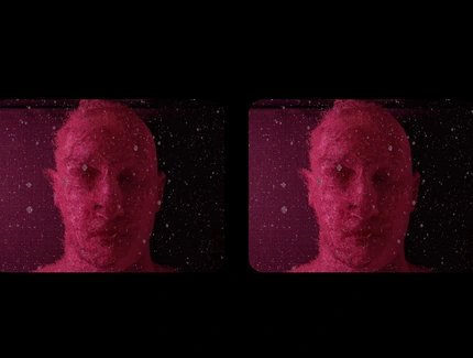 Video still: Frontalansicht einer Person mit geschlossenen Augen in einer Art Flüssigkeit. Das Still zeigt die selbe Ansicht zweimal nebeneinander und pink eingefärbt. Um beide Fenster herum liegt ein schwarzer Rahmen.