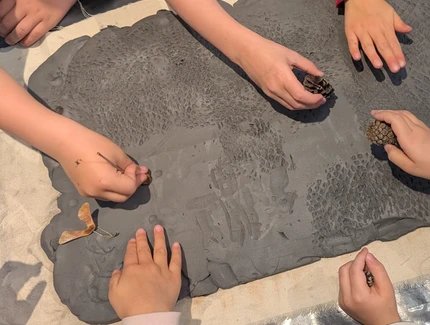 Experimentieren mit Ton: Kinderhände machen Muster in eine Tonschicht