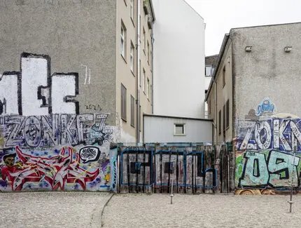 Zwei Häuser und zwischen ihnen ein Zaun. Alles ist mit bunten Graffiti bedeckt.