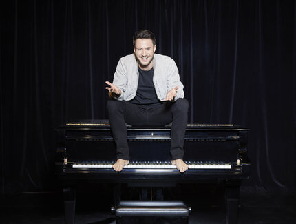 Florian Wagner sitzt auf einem Klavier auf einer schwarzen Bühne