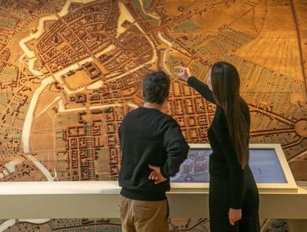 Besucherin und Besucher vor einem Stadtmodell mit Medienstation