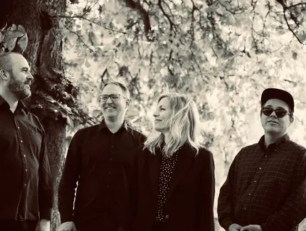 Die Band steht unter einem Baum, die Gesichter fröhlich