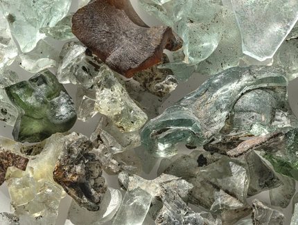 Zerbrochene Glasscherben in verschiedenen Formen und Farben, darunter grün, braun und klar, mit rauen und glatten Oberflächen.