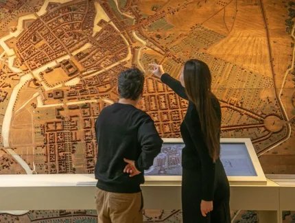 Besucherin und Besucher vor einem Stadtmodell mit Medienstation