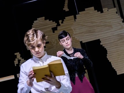 Zwei junge Frauen in altmodischen Kostüumen lesen jede in einem Buch. Die eine Frau ist im Vordergrund des Bildes und unscharf. Die zweie Frau steht weiter im Hintergrund und ist klar zu erkennen.