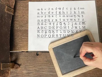 Eine Person schreibt mit einem Griffel auf einer Schiefertafel