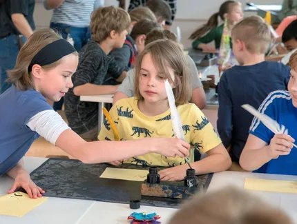 Kinder im Museumslabor schreiben mit Tinte und Feder
