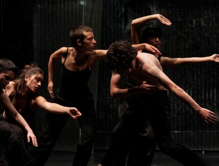 Fünf schwarzgekleidete junge Menschen vollführen Bewegungen auf einer dunkel ausgeleuchteten Bühne.