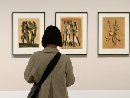 Foto: Rückenansicht einer Person mit kurzem Bob, die vor drei Zeichnungen von Hans Uhlmann steht.