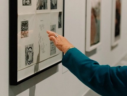Eine Hand deutet auf ein Detail in einer gerahmten Collage von Raoul Hausmann, die an der Wand hängt.