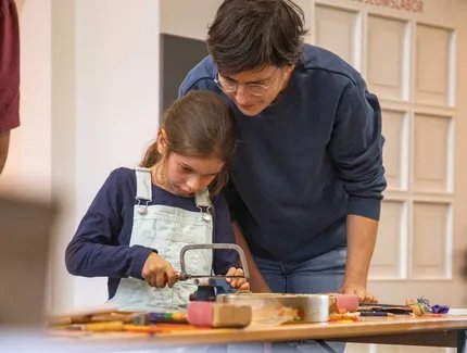 Mann und Kind beim gemeinsamen Sägen für ein Musikinstrument im Museumslabor
