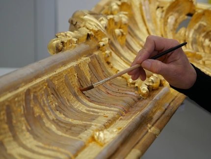 Rahmenrestaurierung, eine Hand führt einen Pinsel, mit dem Blattgold auf einem Bilderrahmen glattgestrichen wird