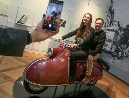 Zwei Besucher:innen beim "Foto-Shooting" auf dem Motorroller.