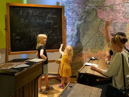 In der Ausstellung BerlinZEIT spüren Eltern mit Kindern umgeben von historischem Mobiliar den Schulalltag der Kaiserzeit nach.