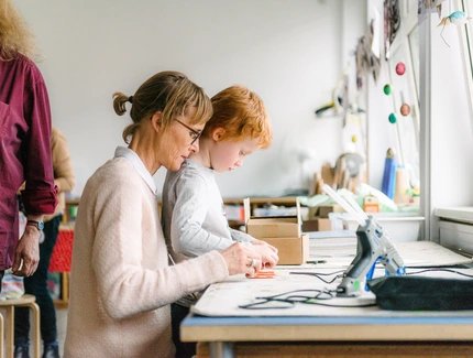 Eine erwachsene Person und ein Kind sitzen an einem Werktisch im Atelier Bunter Jakob und toben sich kreativ aus.