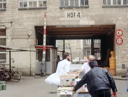 Drei Männer schieben eine mit Kisten beladene Karre durch einen Hinterhof