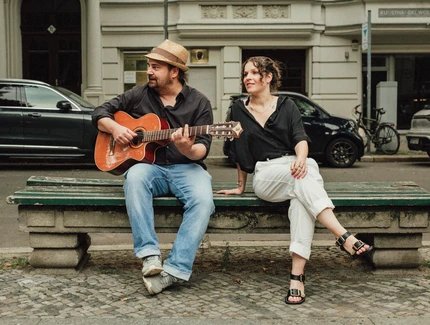 Anne Helm und Marcel Weller mit Gitarre sitzen auf einer Bank.
