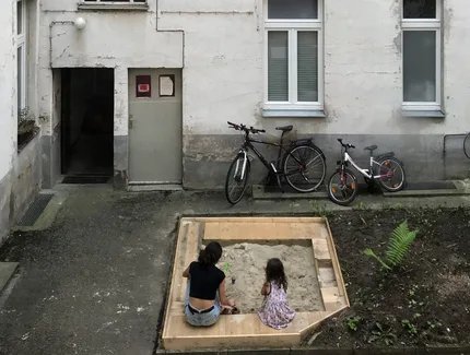 Frau mit Kind im Sandkasten eines Berliner Hinterhofs