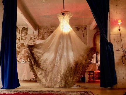 Ein Brautkleid hängt als Leuchte von der Deckenwand