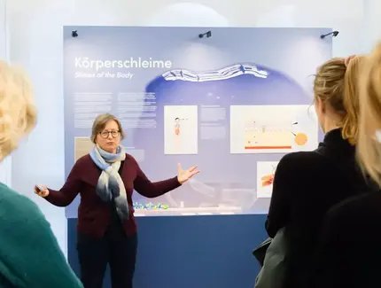 Vermittlerin vor Ausstellungswand Körperschleime