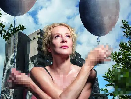 Katja Riemann sitzt unbekleidet in der Hocke vor einem Plattenbau und hält jeweils einen gräulichen Luftballon in den Händen. Die Hände, der Brust- und Intimbereich sind verpixelt.