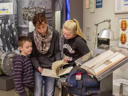 Eine Familie steht in der Ausstellung "Alltag in der DDR" und betrachtet gemeinsam ein Objekt.