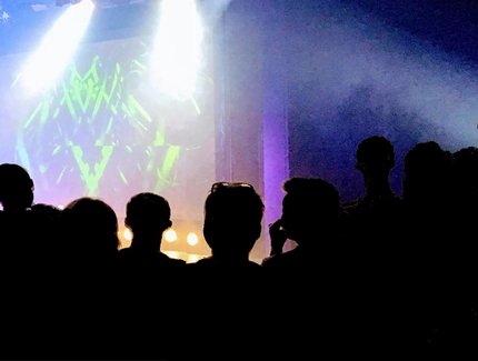 GRAFIK Menschen vor einer beleuchteten Bühne