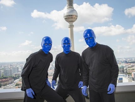 Die BLUE MAN GROUP posiert vor dem Fernsehturm bei strahlend blauem Himmel.