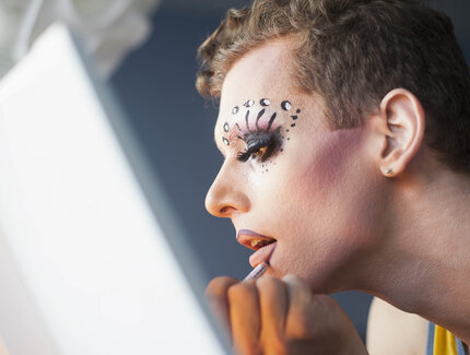 Drag queen doing make up in front of a mirror
