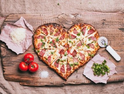 Heart-shaped pizza and ingredients on cutting board