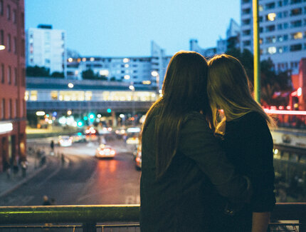 Lesbisches Paar umarmt sich und guckt in Richtung Stadt