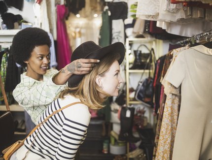Ladenbesitzerin probiert Hut auf Kundin in Vintage Boutique