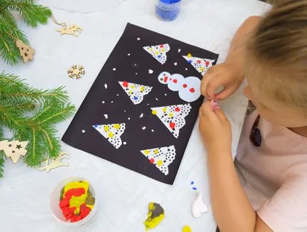 Junges Mädchen bastelt Weihnachtskarte mit Schneemann und Weihnachtsbaum aus Vogelperspektive