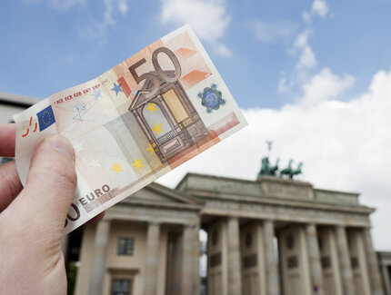 50-Euro-Schein wird vor dem Brandenburger Tor in die Luft gehalten