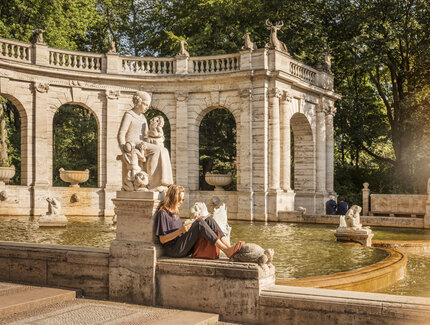 A woman reads at the fairytale fountain in the Volkspark Friedrichshain
