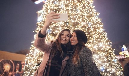 Girlfriends doing selfie in front of christmas tree.