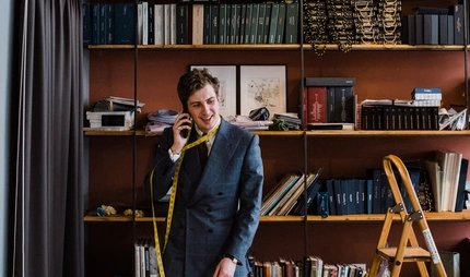 Maximilian Mogg am Telefon, mit einem mit einem Maßband um den Hals, in seinem Laden in Berlin