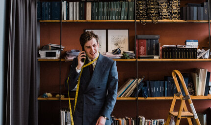 Maximilian Mogg am Telefon, mit einem mit einem Maßband um den Hals in seinem Laden in Berlin.