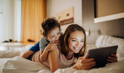 Mother and child lying on a bed and look at pictures on a tablet