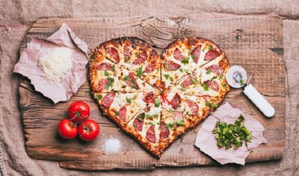 Heart-shaped pizza and ingredients on cutting board