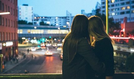 Lesbisches Paar umarmt sich und guckt in Richtung Stadt