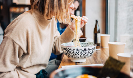 A young woman eats ramen soup at a counter in Berlin