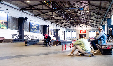 Skatehalle Berlin: Zwei Skater schauen Rollstuhlskater zu