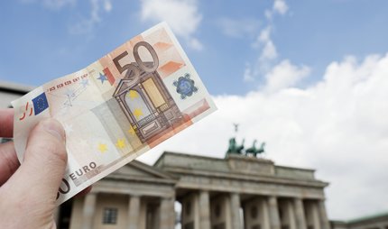 50-Euro-Schein wird vor dem Brandenburger Tor in die Luft gehalten